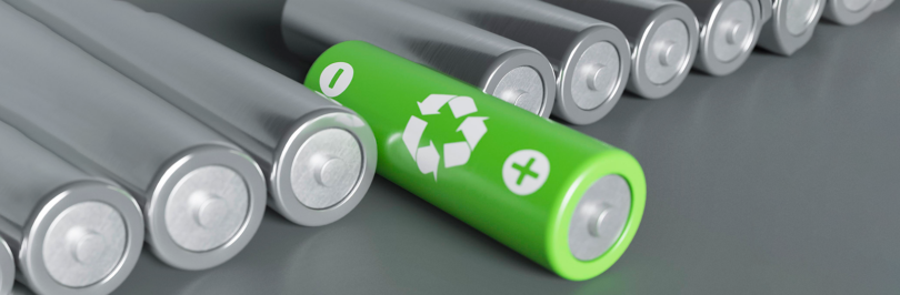 Used batteries lined up on table with one green recyclable battery