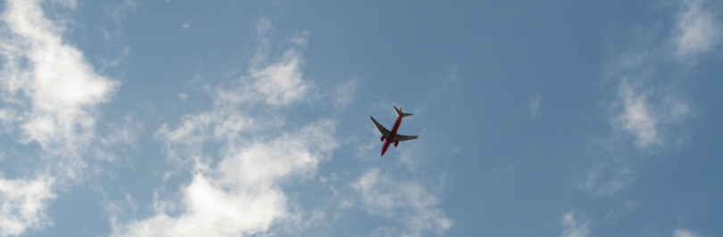 underside-of-airplane-flying-in-cloudy-blue-sky