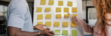 two individuals planning with post-it notes on a white board