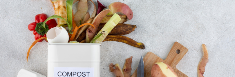 food waste spilling out of a compost bin next to a chopping board holding a potato