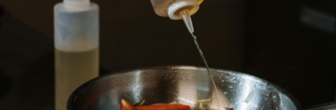 a person pouring oil into a pan with vegetables