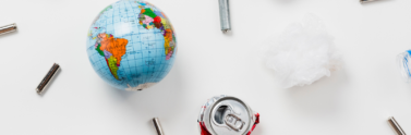 Various items including a globe, a used soda can, plastic, and other recyclable items on a white surface