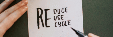 A hand holding a sign that reads reduce, reuse, recycle