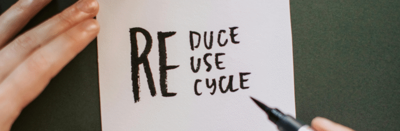 A hand holding a sign that reads reduce, reuse, recycle