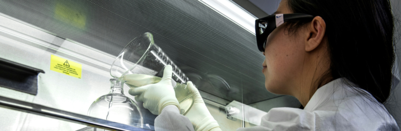 A lab technician holding a beaker and pouring into another apparatus.