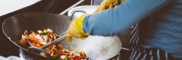 someone wearing yellow gloves cooking in a wolk