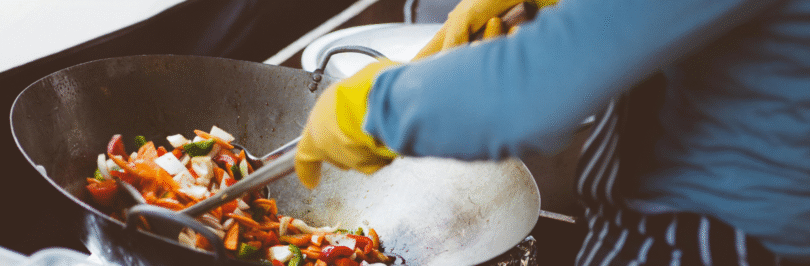 someone wearing yellow gloves cooking in a wolk