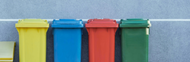 Four bins on the street with the colours yellow, blue, red, and green respectively