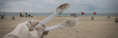 Hand holding plastic cutlery at the beach