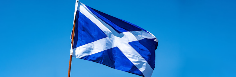 Scottish flag flying on flagpole with blue sky