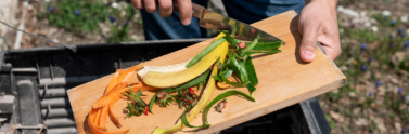 Close up of person putting food scraps from cutting board into compost bin