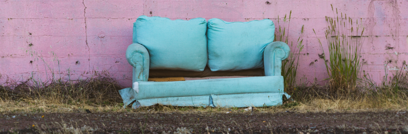 Abandoned couch outside in front of a pink wall