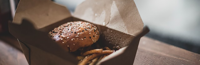 Burger in single-use takeout container on table