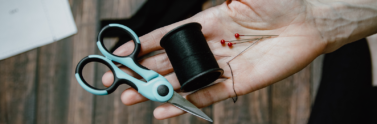 Person holding sewing scissors, black thread, and pins