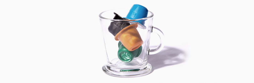 Assorted coffee capsules in a glass mug with a white background