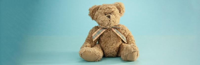 Brown teddy bear with bow sitting on plain blue background