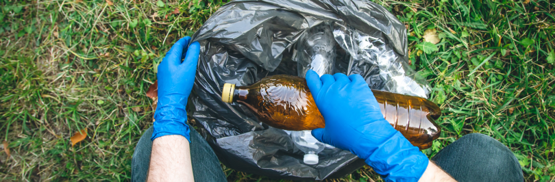 Person wearing gloves placing a plastic bottle into a black garbage bag