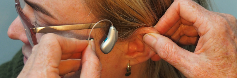 Person putting hearing aid on another persons ear
