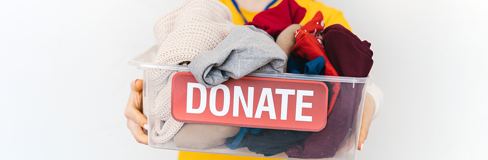 Person holding clear donation bin with old assorted clothes