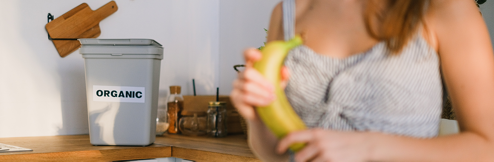 Person in kitchen holding a banana with organic bin