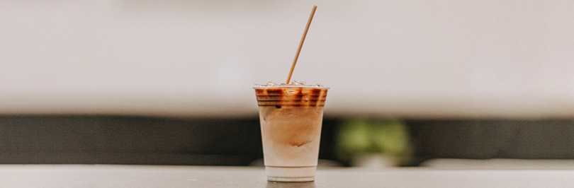 Coffee in disposable cup with straw on wooden table