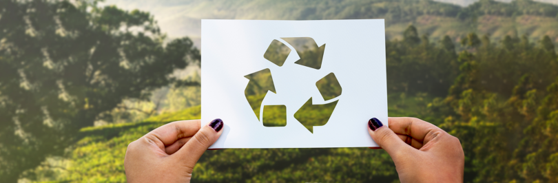Person holding up paper with recycling arrows in nature