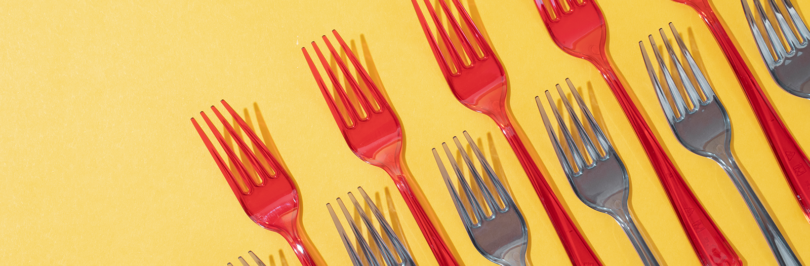 Black and red single-use plastic forks on yellow background
