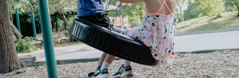 Two children swinging on tire swing on a playground